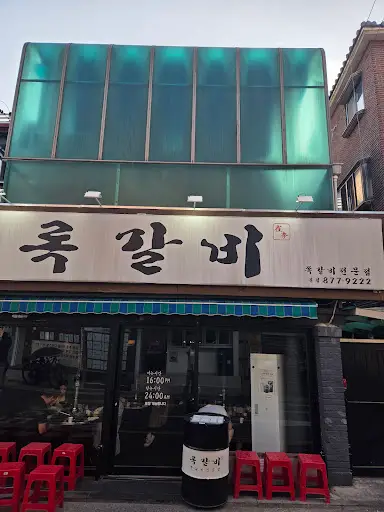 건물 외관 모습. 투명한 녹색 지붕과 간판이 보입니다.