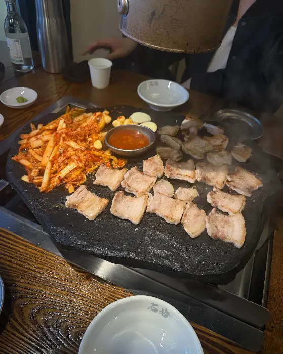 달궈진 돌판 위에 지글지글 구워지는 삼겹살과 김치의 모습
