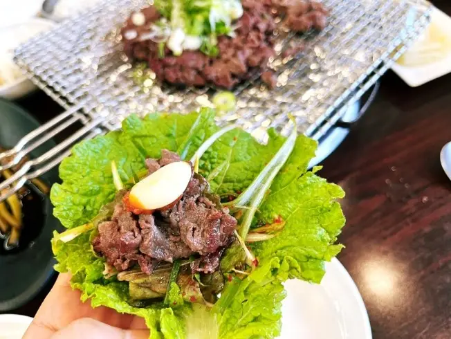 상추쌈에 얹어진 불고기 한 점. 마늘과 쌈장이 곁들여져 완성된 모습.