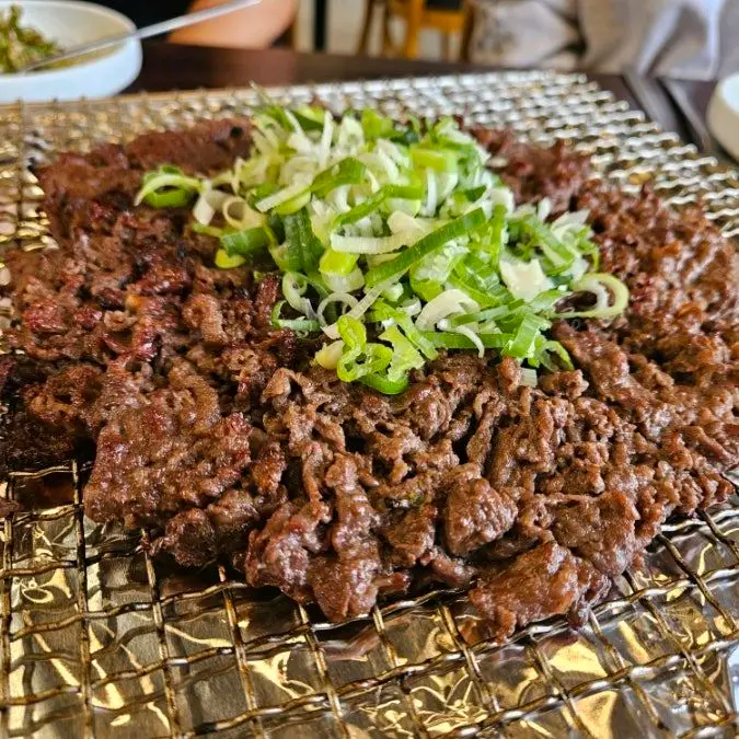 석쇠 위에서 푸짐하게 구워진 언양 불고기. 얇게 펴진 고기 위에 파채가 얹어져 있다.