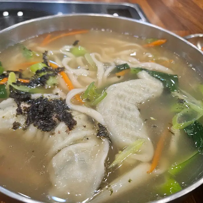 김이 모락모락 나는 해물 칼국수 냄비, 젓가락으로 면을 건져올리고 있다.