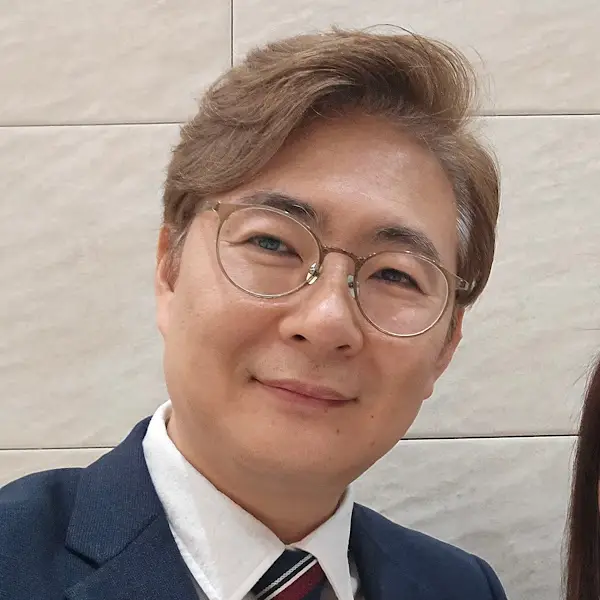 안경을 쓴 남성이 부드럽게 미소 짓는 모습