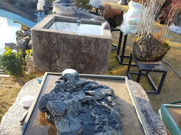 돌로 만들어진 작은 연못과 그 위에 놓인 석물, 주변으로 돌과 나무들이 배치된 모습