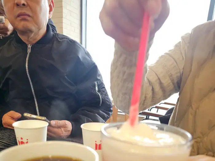 Close-up of a person stirring a pink drink with a red straw, with other drinks and people in the background