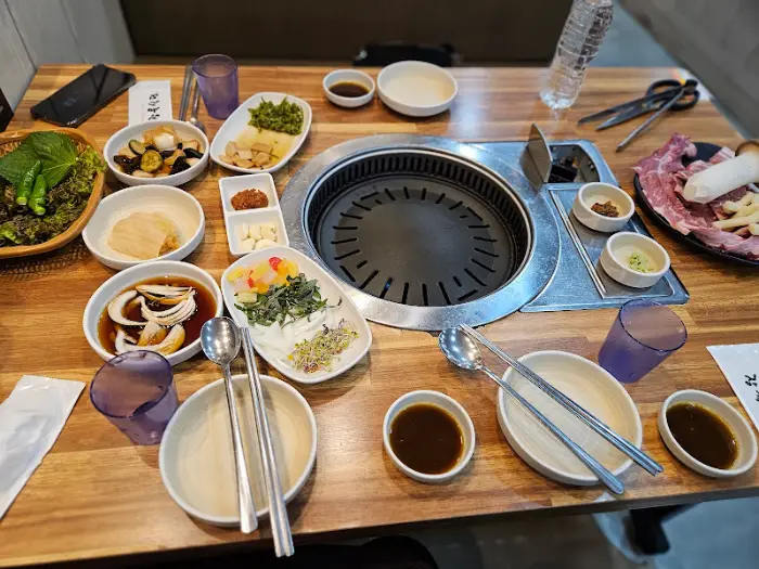 테이블 위 풍경. 불판, 밑반찬, 쌈 채소, 소스 등이 세팅되어 있다.