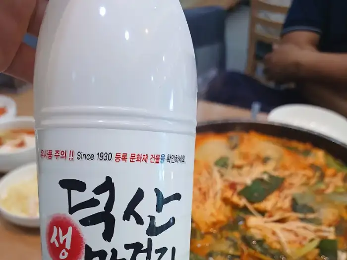 '덕산 생 막걸리' 병이 매운탕 냄비 옆에 놓여 있는 모습