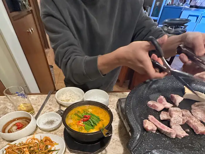 직원이 가위로 고기를 자르는 모습과 옆에 놓인 찌개