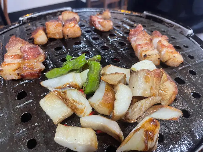 잘 구워진 삼겹살과 목살, 그리고 버섯과 꽈리고추가 불판 위에 놓여 있는 모습