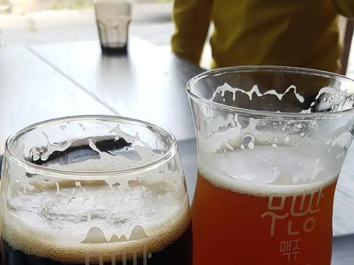 수제 맥주 두 잔이 놓여 있는 사진, 거품이 풍성하게 올라와 있습니다.