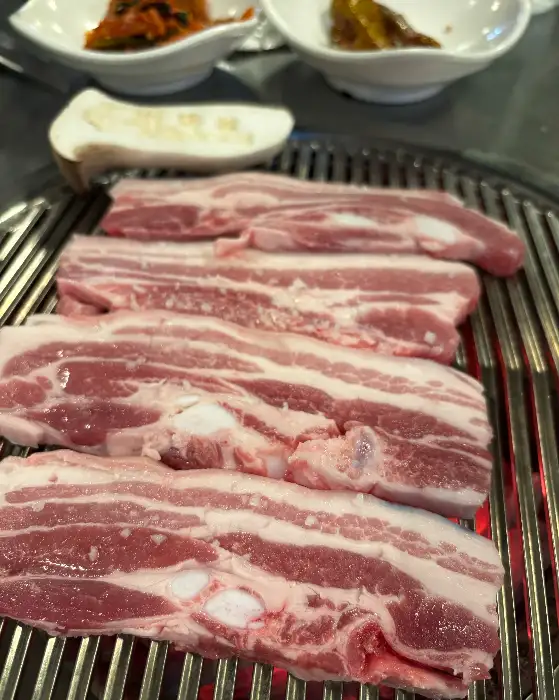 두툼한 흑돼지 삼겹살과 목살이 숯불 위에서 익고 있는 모습. 층층이 쌓인 지방과 살코기의 비율이 이상적이다.