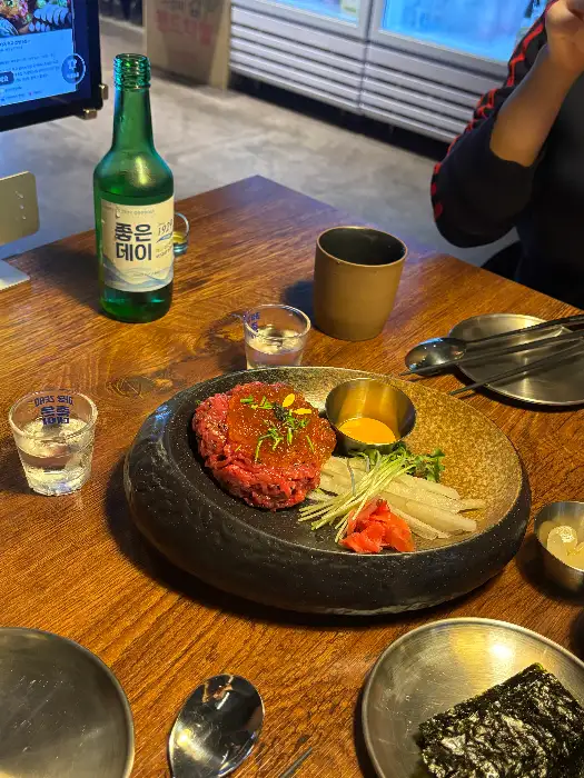 육회가 담긴 접시와 술병, 잔이 놓인 모습