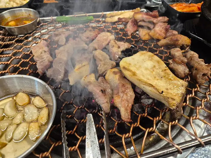 숯불 위에서 다양한 고기 부위와 멜젓이 함께 익어가는 모습