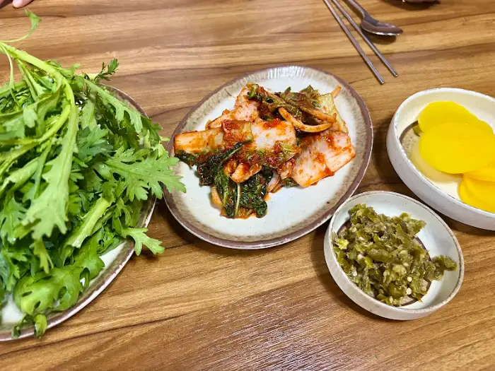 테이블 위에 놓인 김치, 깍두기, 그리고 신선한 쑥갓 등의 반찬들.