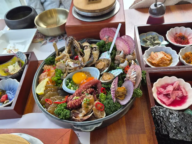 해물장 정식 전체 모습. 중앙에 해물장이 있고, 주변에 솥밥과 반찬이 놓여 있다.