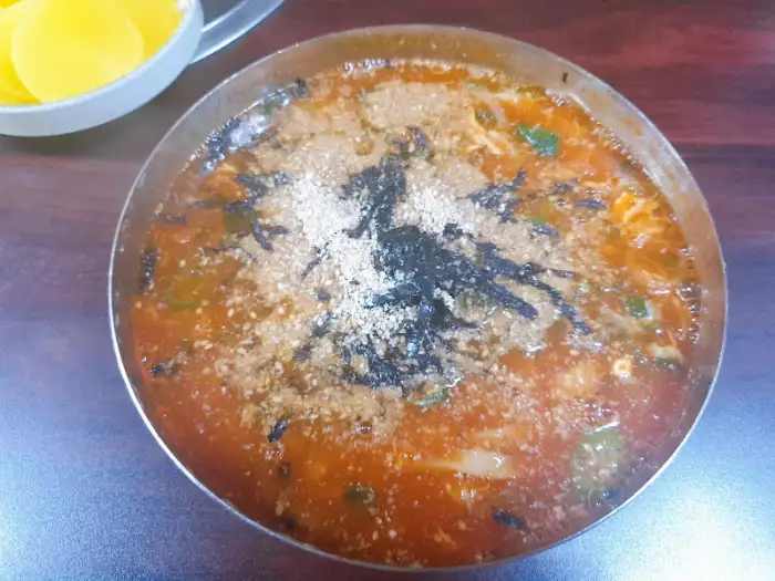 그릇에 담긴 칼국수 전체 모습, 국물이 붉고 진한 색을 띠며 위에 김가루와 깨가 뿌려져 있다.