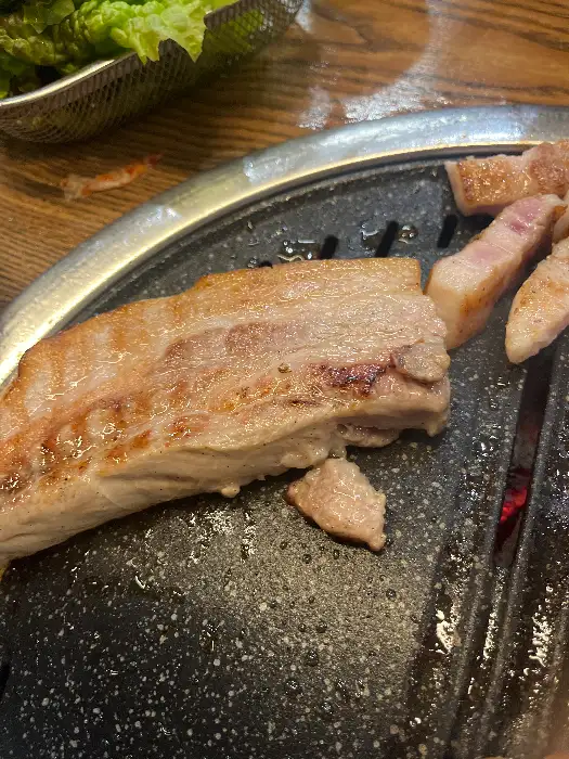 불판 위에서 먹음직스럽게 익어가고 있는 삼겹살의 모습. 기름기가 흘러내리며 윤기가 돈다.