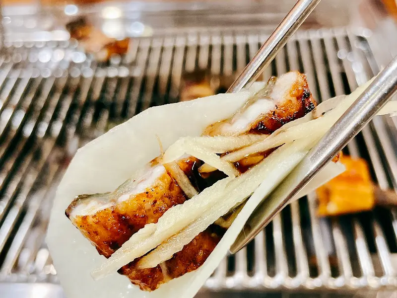 장어 한 점을 백김치와 생강채를 곁들여 젓가락으로 집어 올리는 모습