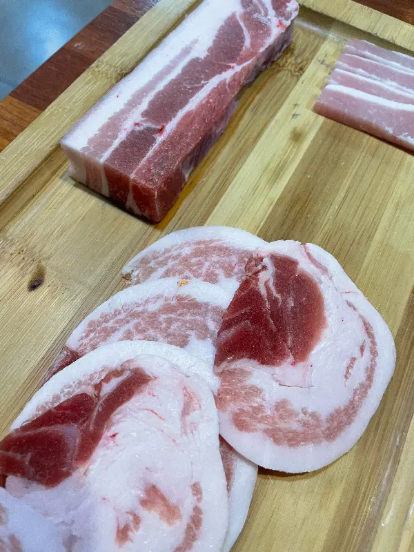 신선한 흑돼지 오겹살이 나무 도마 위에 놓여 있다. 선명한 붉은 색과 하얀 지방의 조화가 인상적이다.