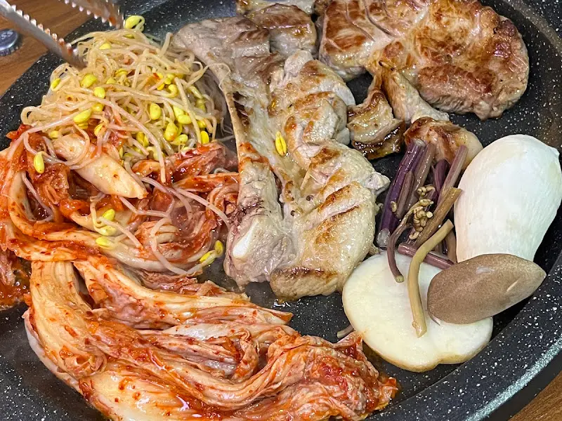 돌판 위에 다양한 부위의 고기와 김치, 콩나물이 함께 구워지고 있는 모습