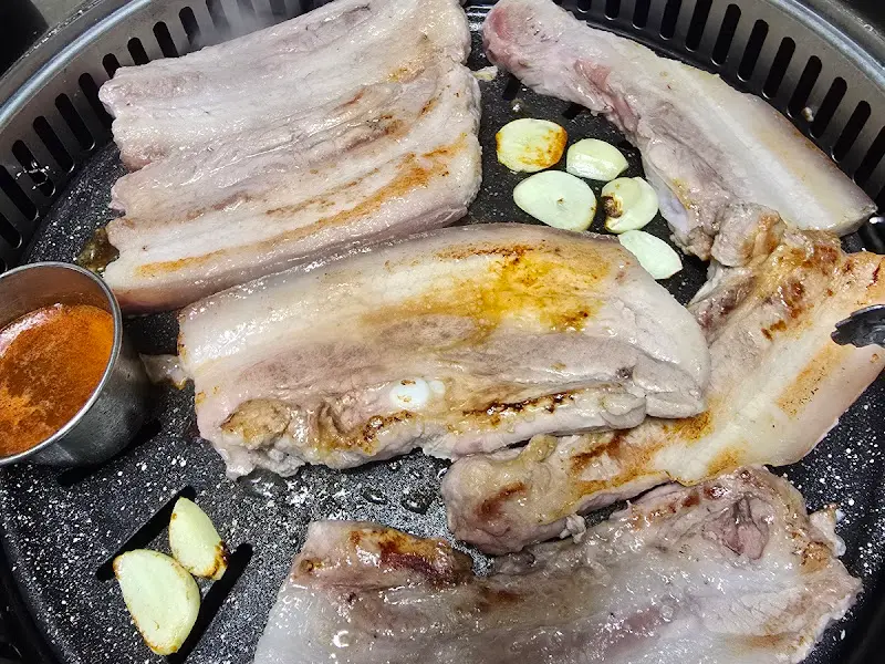 불판 위에서 구워지는 두툼한 흑돼지 삼겹살