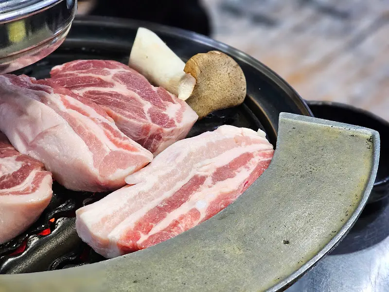 숯불 위에서 익어가는 두툼한 돼지 목살과 새송이버섯