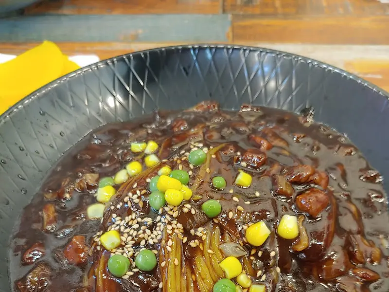 윤기가 흐르는 짜장면 위에 옥수수와 완두콩이 톡톡