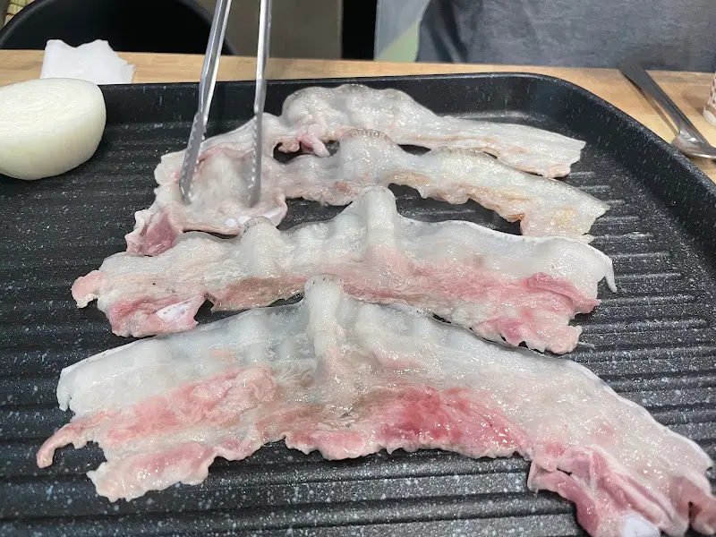 집게로 돼지고기를 불판 위에 올리는 모습