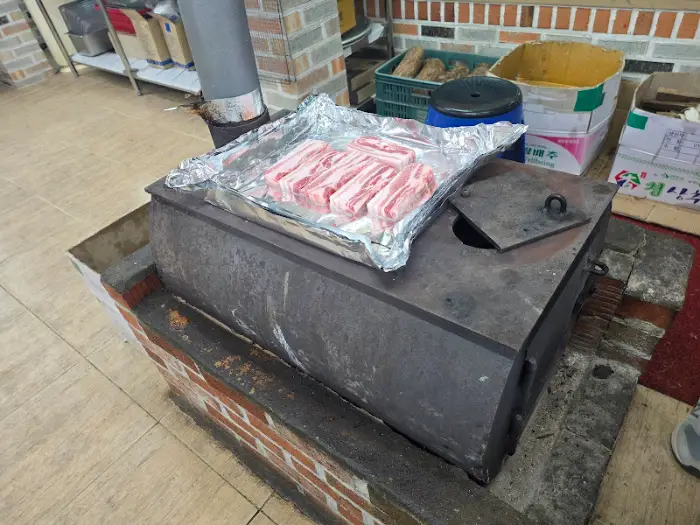 장작 난로 위에 알루미늄 호일이 깔려있고, 두툼한 삼겹살이 놓여있다.