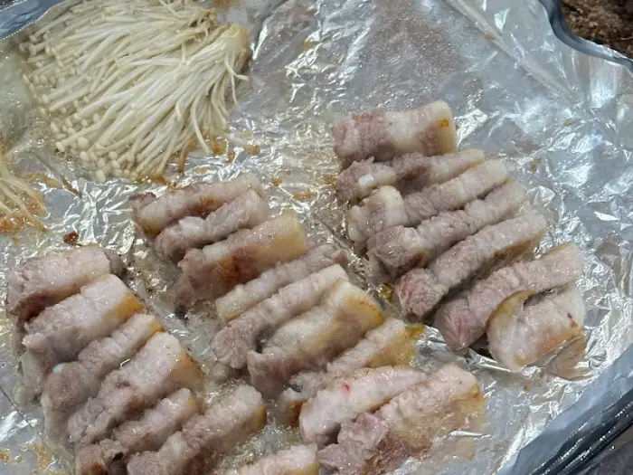 잘 익은 삼겹살과 팽이버섯, 콩나물이 불판 위에 놓여있다.