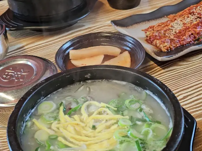 식탁에 차려진 소머리국밥과 반찬들. 깍두기와 김치, 그리고 곁들여 먹을 수 있는 무생채가 보입니다.