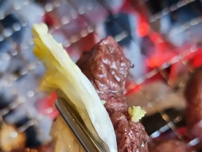 집게로 고기 한 점을 집어 쌈 채소에 올리는 모습