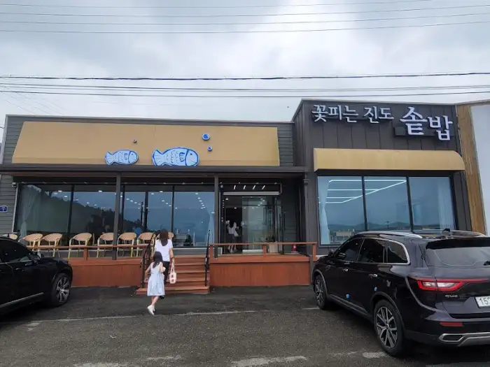 식당 외관, 밤에 조명이 켜져 있으며, '꽃피는 진도 솥밥'이라는 간판이 보인다.