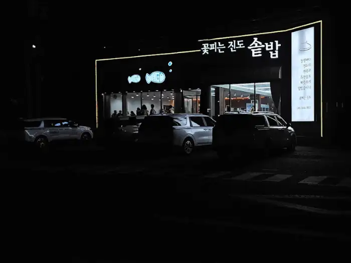 식당 외관, 밤에 조명이 켜져 있으며, '꽃피는 진도 솥밥'이라는 간판이 보인다.