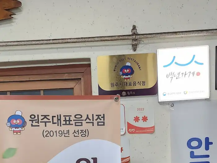 벽에 걸린 '백년가게' 현판과 '원주대표음식점' 인증 간판들.