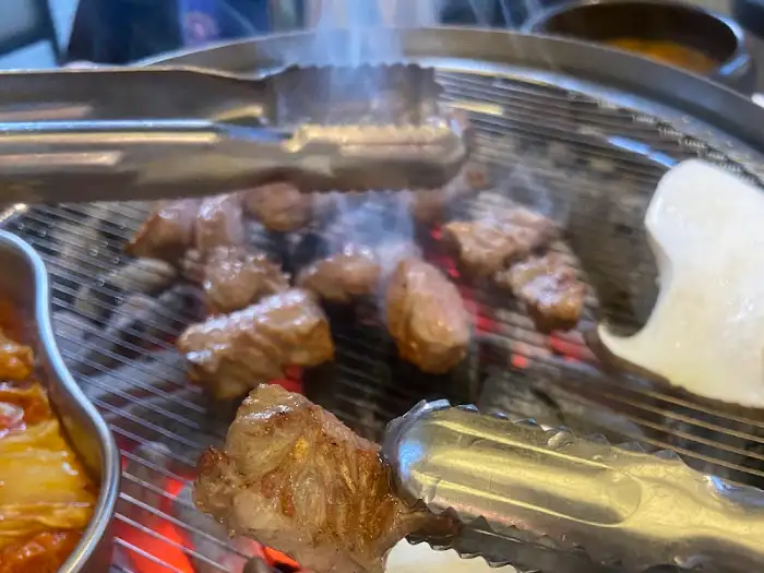 집게로 집어지고 있는 숯불에 구워지는 돼지고기