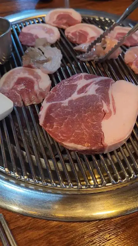 불판 위에서 맛있게 구워지고 있는 흑돼지 오겹살의 모습.