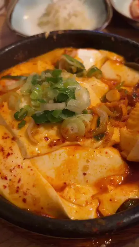 해물 순두부 찌개가 담긴 검은 뚝배기 클로즈업 사진. 큼지막한 순두부와 파가 보인다.