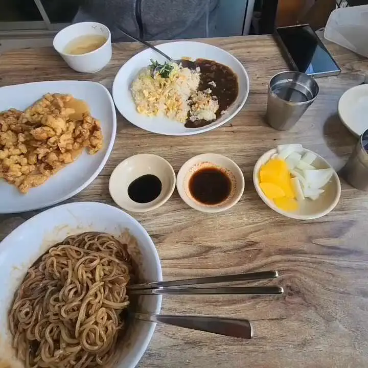 테이블 위에 놓인 짜장면, 탕수육, 단무지, 양파 등의 모습