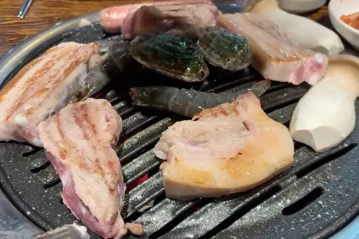 불판 위에 흑돼지, 해산물, 버섯 등이 다양하게 올라가 있는 모습