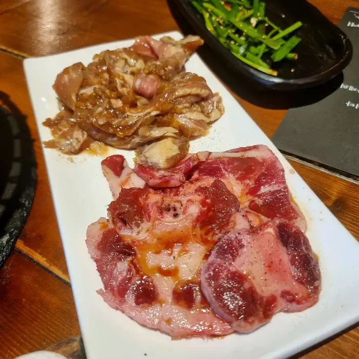 팬 위에 먹음직스럽게 구워지고 있는 양념 소갈비살과 함께 마블링 좋은 생 소고기 부위