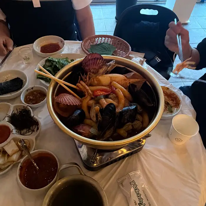 새우, 오징어, 조개 등 해산물이 푸짐하게 담긴 조개탕 혹은 해물찜으로 추정되는 요리. 붉은 국물이 베이스이며, 다양한 채소와 함께 끓여지고 있다.