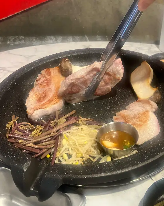 집게로 집어 올린 구워진 삼겹살 한 점