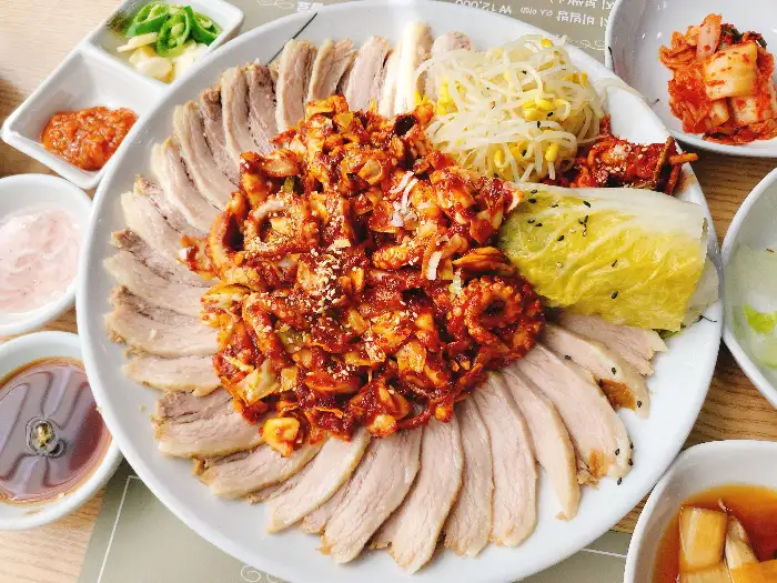 낙지보쌈 메인 요리와 함께 차려진 다양한 밑반찬들. 백김치, 콩나물, 김치 등이 정갈하게 담겨 있다.