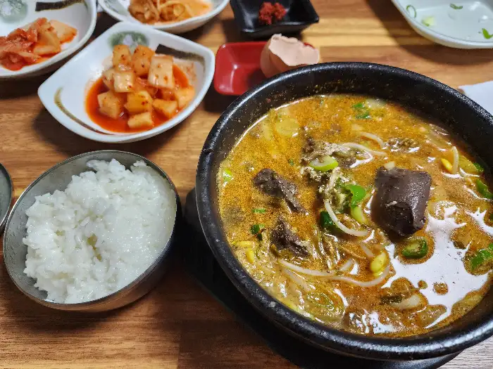국물과 선지가 듬뿍 담긴 선지해장국 뚝배기와 밥, 그리고 깍두기와 김치가 담긴 접시가 보입니다.