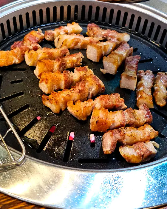 신선한 쌈 채소 위에 삼겹살과 곁들임 재료를 올려 싸 먹는 모습