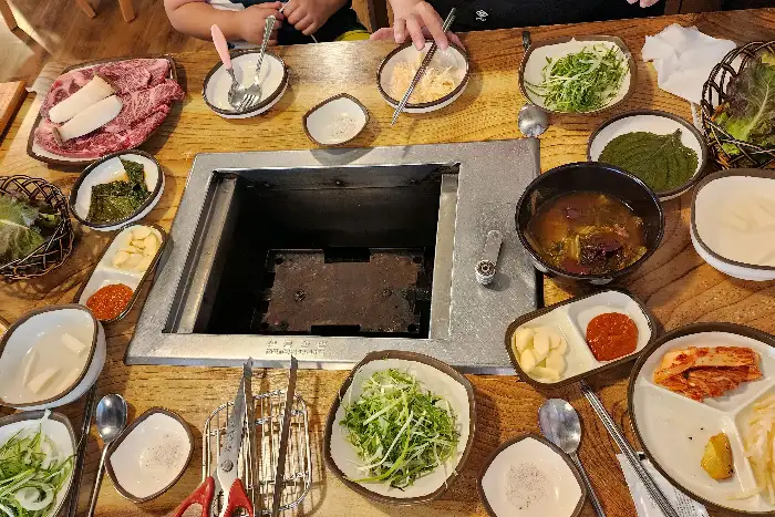 테이블 위에 차려진 다양한 밑반찬과 숯불구이