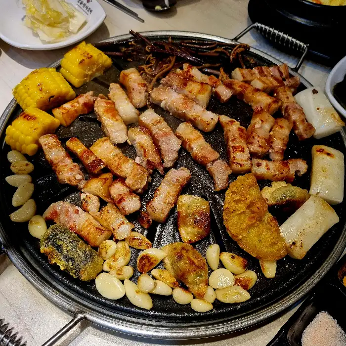 맛있게 구워진 삼겹살, 목살, 돼지갈비와 곁들임 메뉴들이 불판에 가득 찬 모습