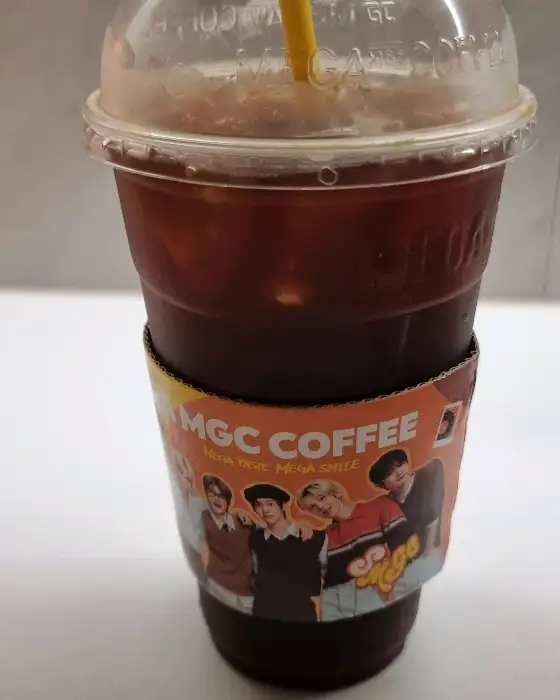 MGC COFFEE 로고와 귀여운 캐릭터들이 그려진 주황색 슬리브가 씌워진 아이스 음료 컵
