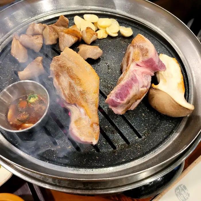 불판 위에서 구워지고 있는 돼지고기와 곁들임 메뉴들