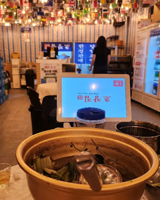 매장 내부의 전반적인 모습. 테이블마다 음식이 차려져 있고, 사람들이 식사를 하고 있으며, 벽에는 메뉴판으로 보이는 종이들이 걸려있다.